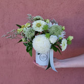 Bouquet of white and green flowers in a box held against a pink wall.