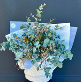 A fresh cut bunch of blue gum and thryptomene flowers, gift wrapped with a ribbon.