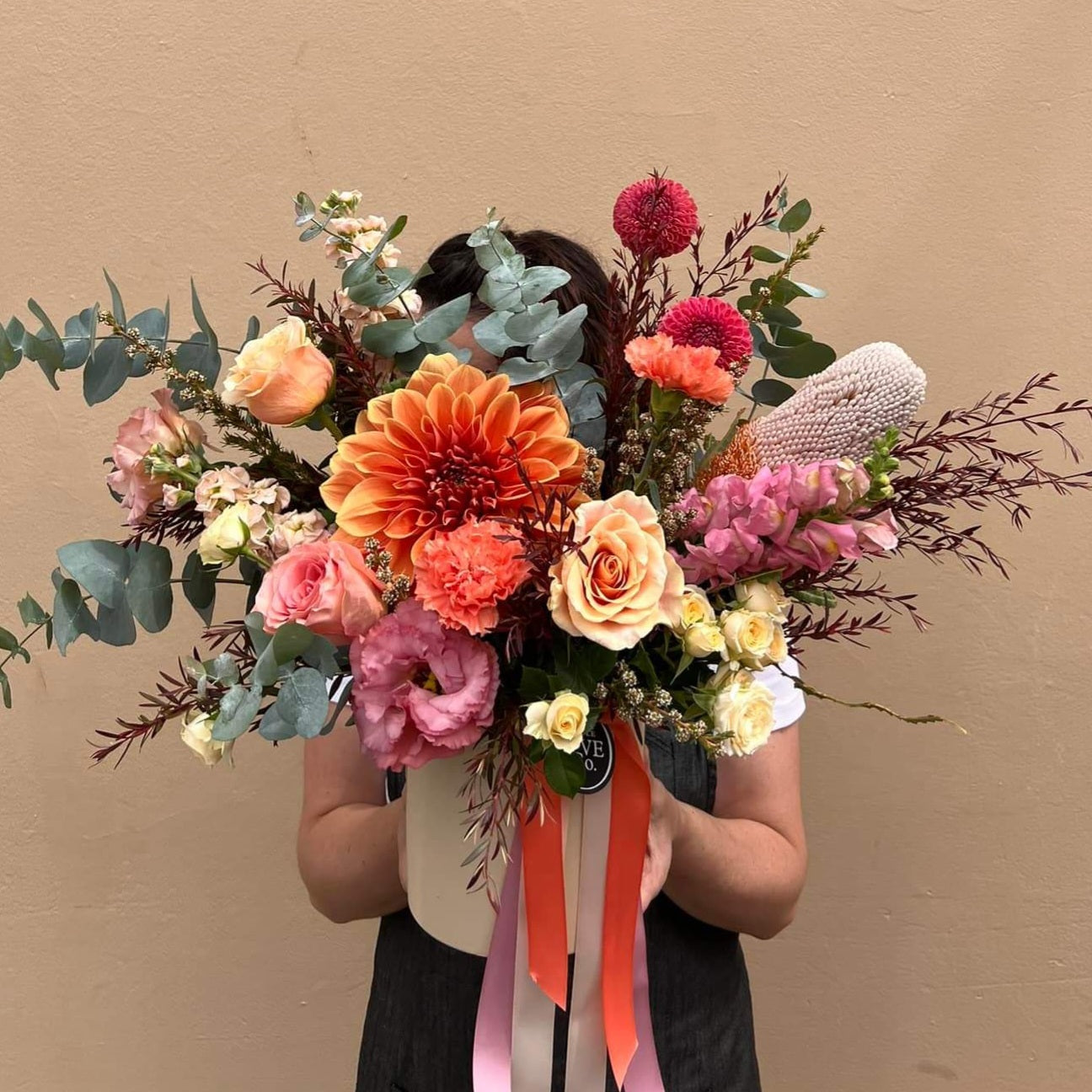 A person holding a modern matte ceramic vessel arranged with a variety of fresh flowers in a range of colors, presented against a neutral background.