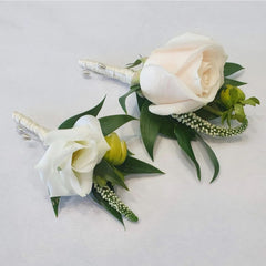 A floral buttonhole featuring a white rose, green leaves, and white ribbon.
