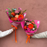 Two bouquets of flowers held by hands against a pink background