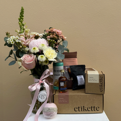 Gift box with flowers, snacks, and a bottle on a beige background