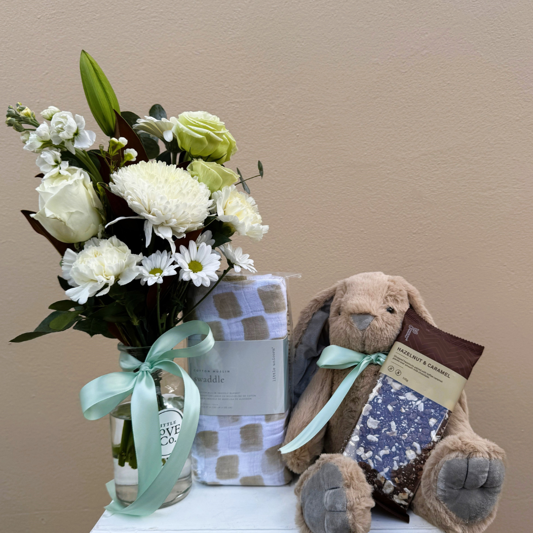Floral arrangement with a vase, a plush toy, and a book on a white surface against a beige background