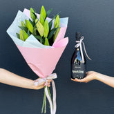 A person holding a bouquet of Asiatic or Oriental lilies in pink wrapping, alongside a bottle of Bird in Hand Sparkling wine.