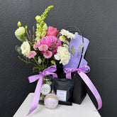 Bouquet of flowers with a black box and bath bomb on a white surface against a dark background