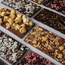 A selection of artisan chocolate bars topped with various ingredients such as nuts, popcorn, and coconut flakes, made by Yours Truly.
