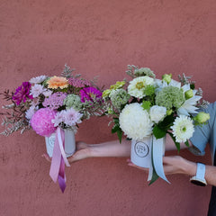 Two ceramic floral arrangements with a mix of seasonal blooms in different colors held against a pink wall.