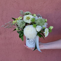 Bouquet of white and green flowers in a box held against a pink wall.