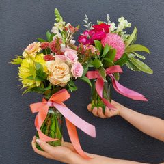 Bouquet of flowers with a pink ribbon held by hands against a dark background