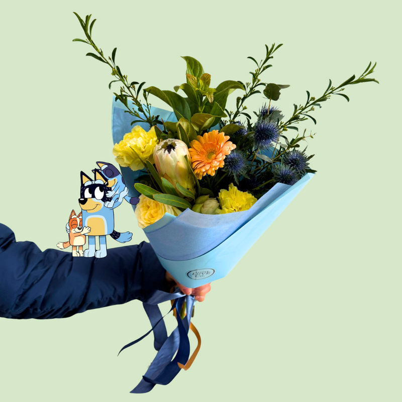 Bouquet of flowers wrapped in blue paper held by a person against a light green background